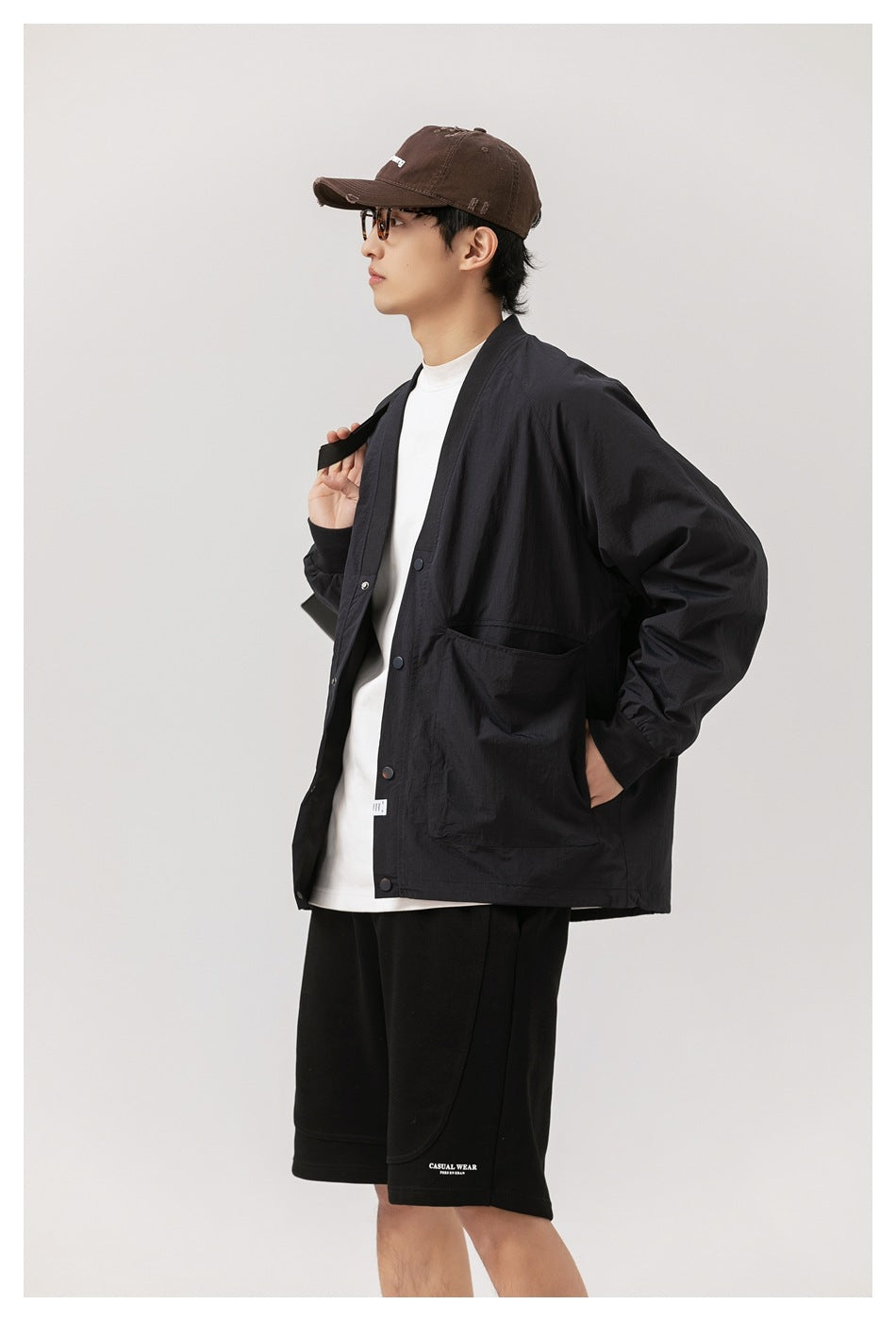 Three-quarter view of a model wearing a black snap-front jacket with roomy pockets and black shorts.