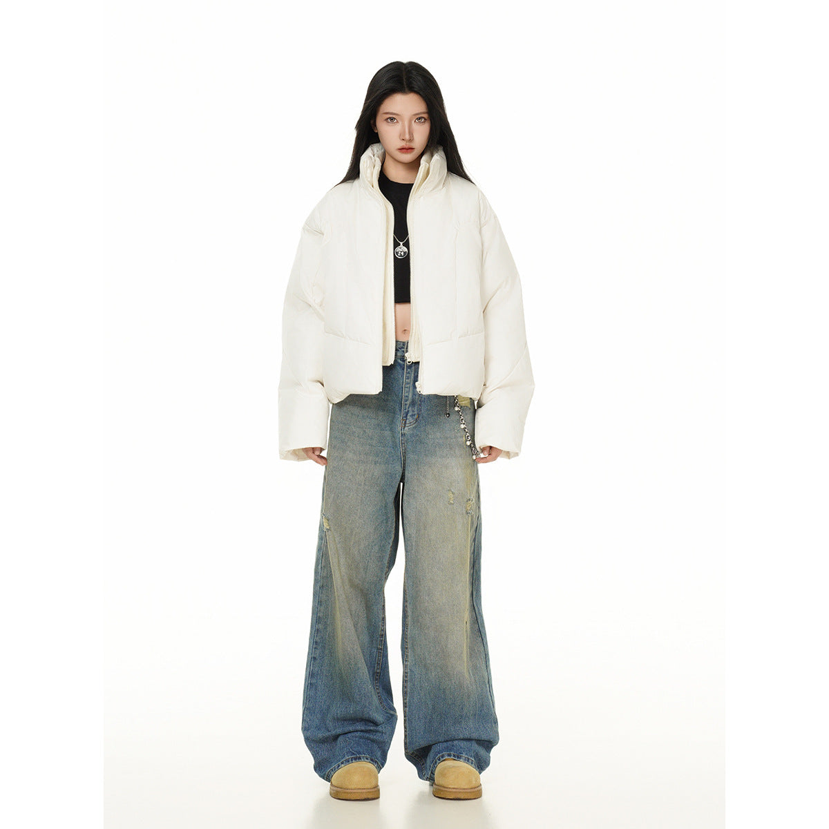 Model wearing an open ivory cropped puffer jacket with a high collar and oversized sleeves, wide-leg jeans, and tan shoes.