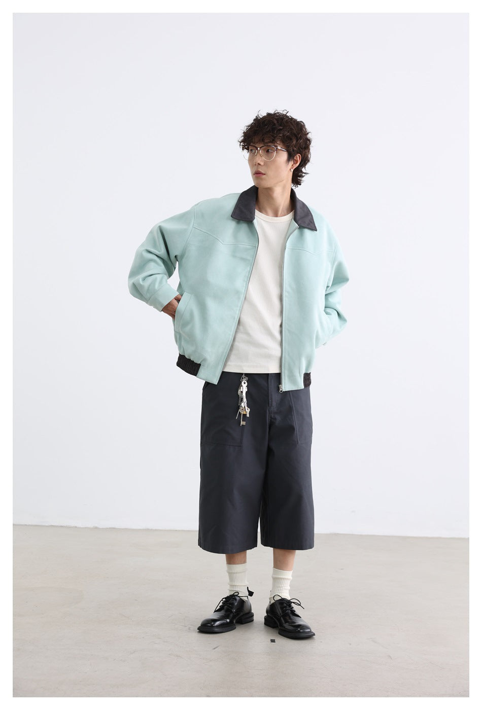 Model wearing a pale mint zip-front jacket with a dark collar and hem, styled with dark shorts.