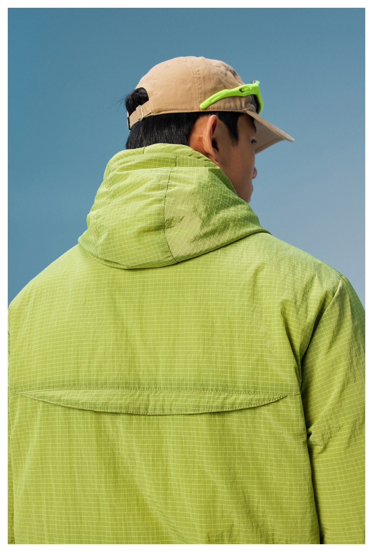 Back view of a model wearing a lime green grid-pattern hooded jacket with a flap across the upper back.