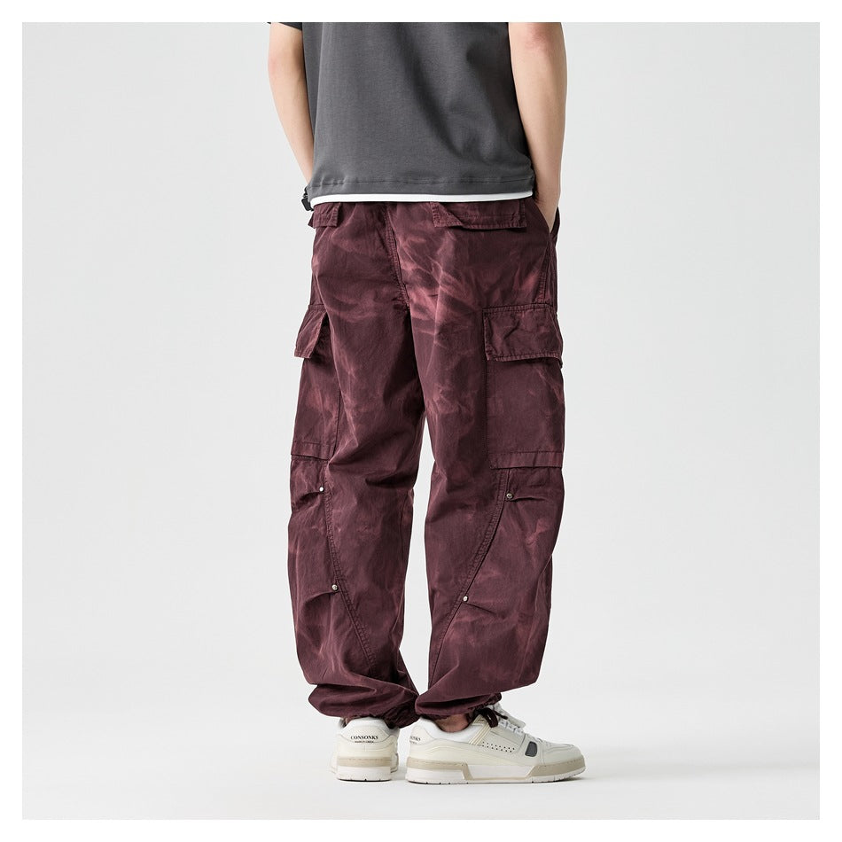 Back view of a model wearing loose burgundy cargo pants with flap pockets and gathered ankle cuffs.