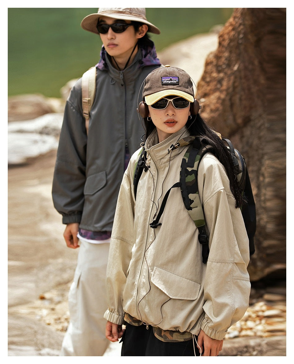 Two hikers model oversized jackets outdoors; a woman wears a cream zip jacket and a man wears a gray jacket.