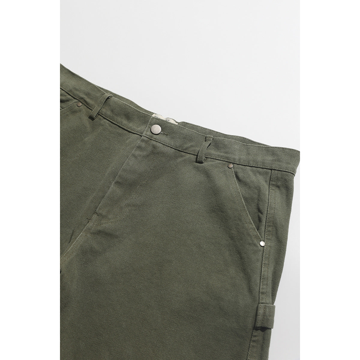 Close-up of olive shorts showing the waistband, button, belt loops, and angled front pocket.