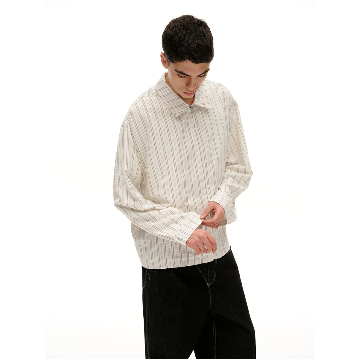 Model adjusts the cuff of a cream shirt with fine vertical stripes, worn with black trousers.