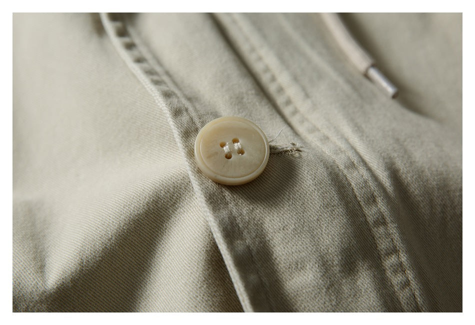Close-up of a cream four-hole button on the stitched placket of a light khaki jacket.