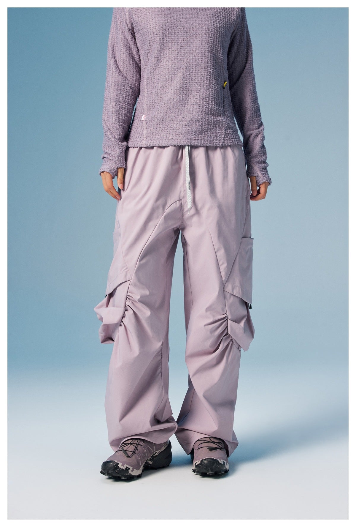 Front view of a person wearing loose lilac cargo pants with a drawstring waist, oversized flap pockets and gathered legs.