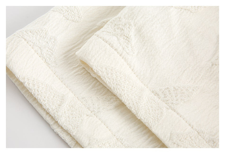 Close-up of layered ivory garment edges with textured bands and raised woven motifs.