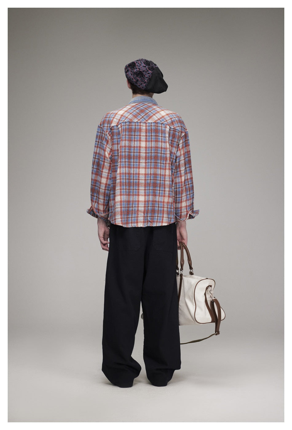 Back view of a model wearing a rust, blue and cream plaid shirt with black trousers and a patterned beret.