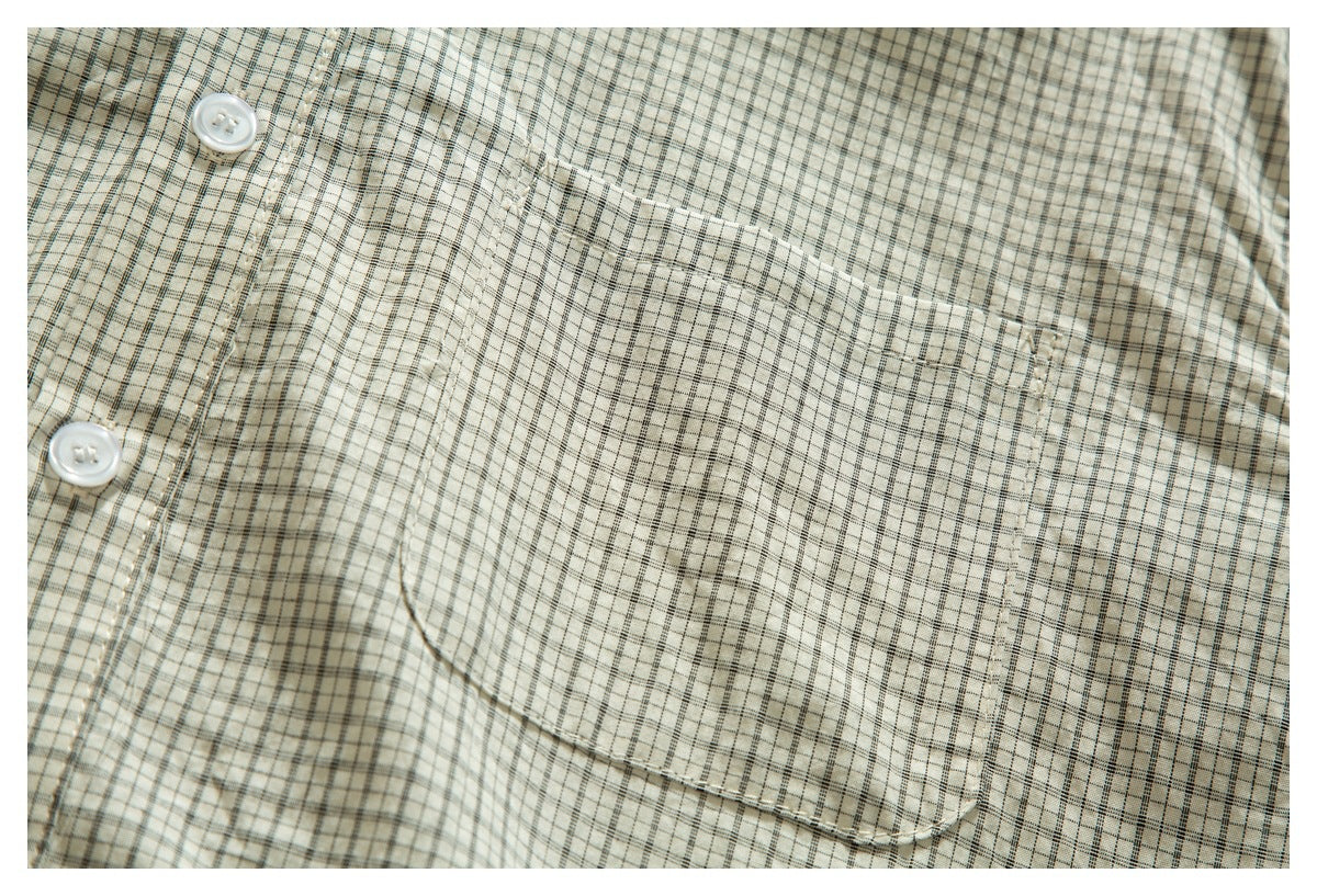 Close-up of a cream shirt with a fine dark plaid pattern, white buttons, and a chest pocket.