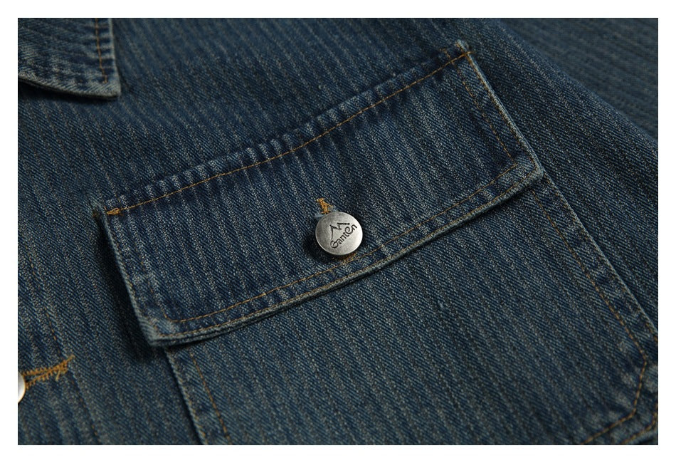Close-up of a dark blue denim jacket's flap pocket, contrast stitching, and metal logo button.