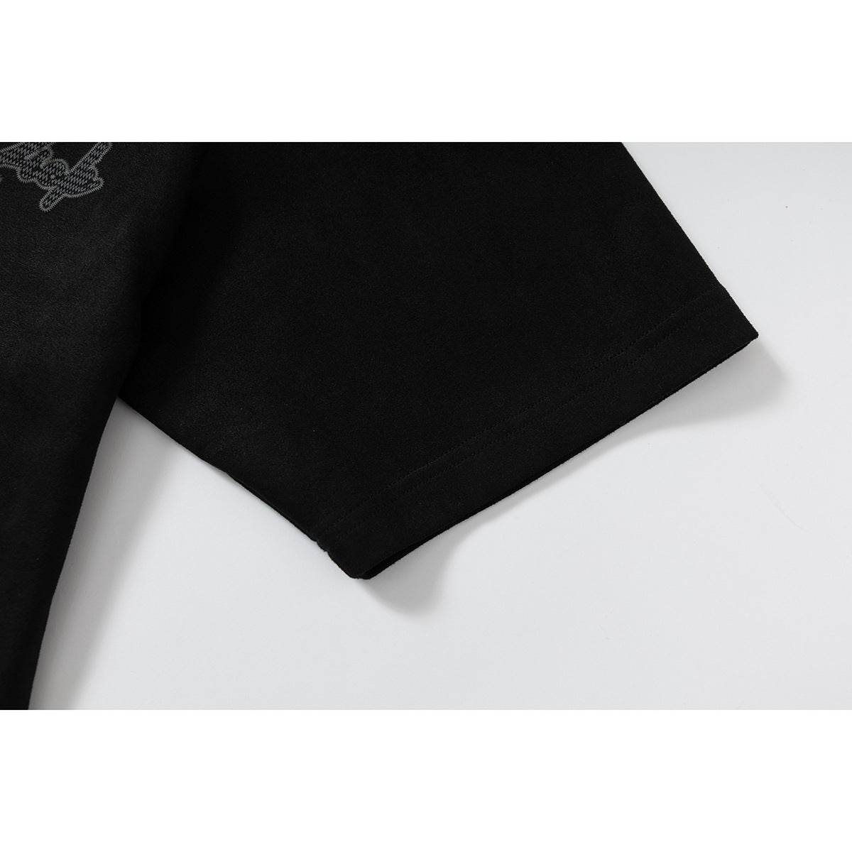 Close-up of a black short sleeve and stitched sleeve hem, with part of an embroidered motif visible.