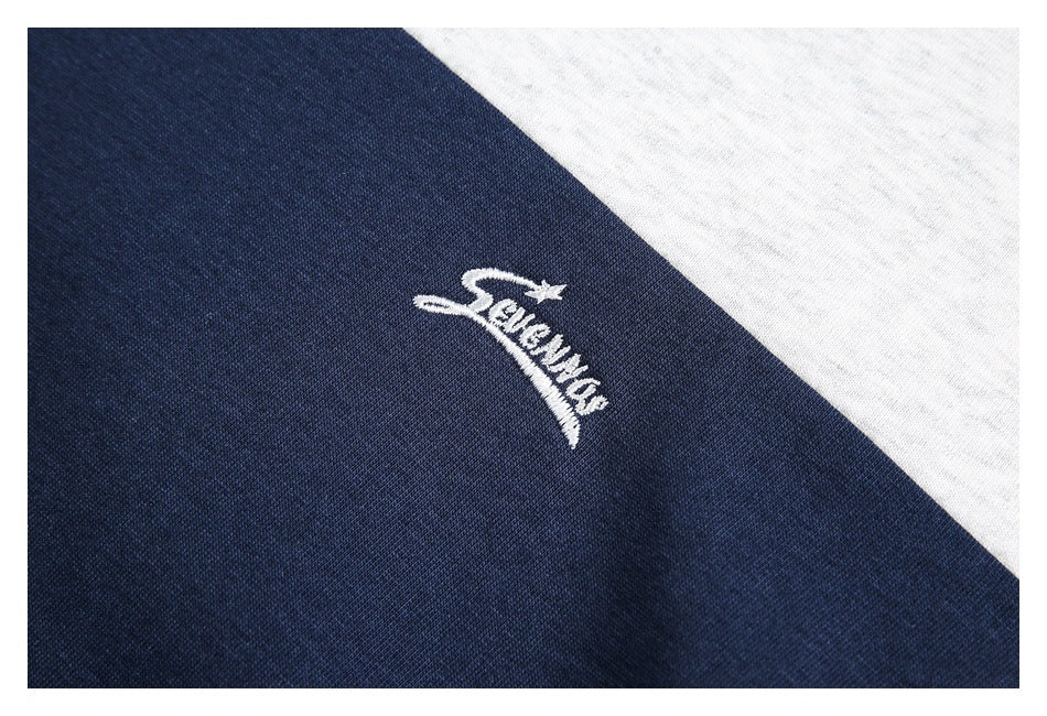 White embroidered script logo on the navy section of a white and navy color-block shirt.