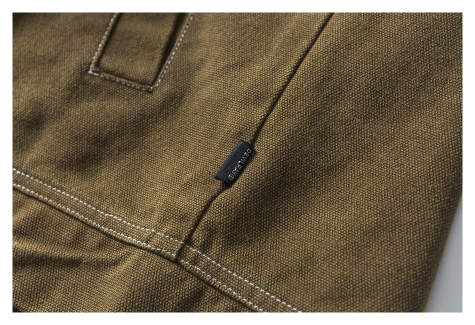 Close-up of olive-brown textured fabric with contrast stitching and a small black sewn-in label.