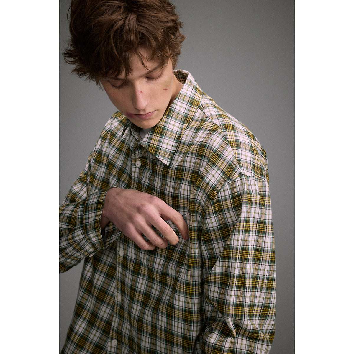 Close-up of a model wearing a white, green, and mustard plaid shirt with a pointed collar and white buttons.