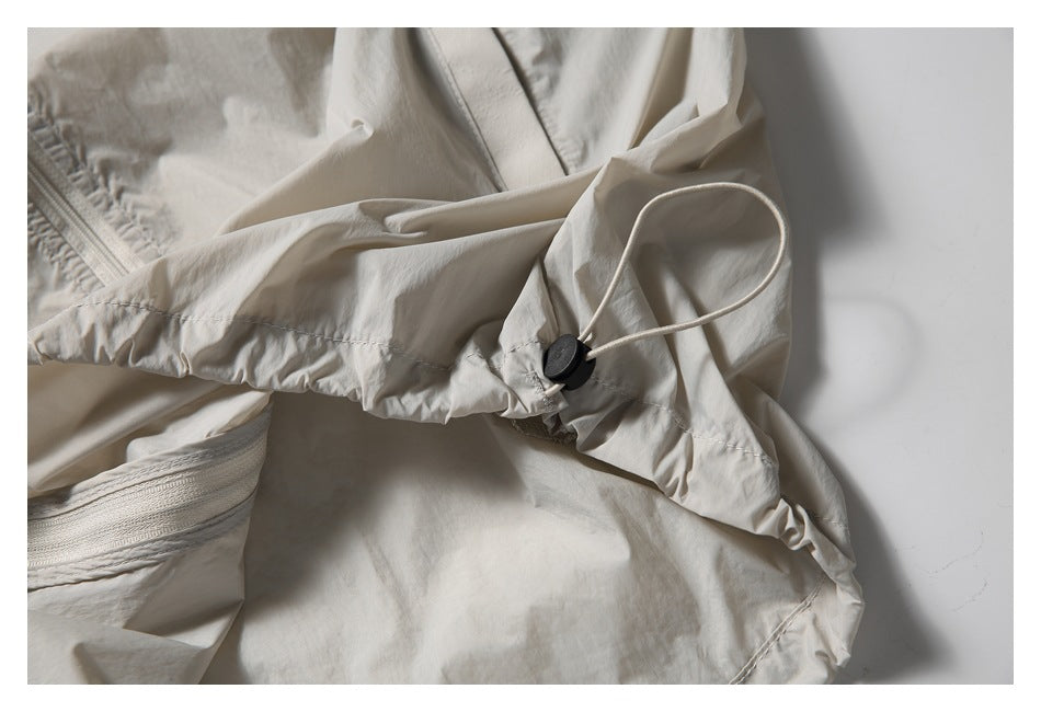 Close-up of a light beige jacket's gathered hood edge and drawcord with a black toggle.