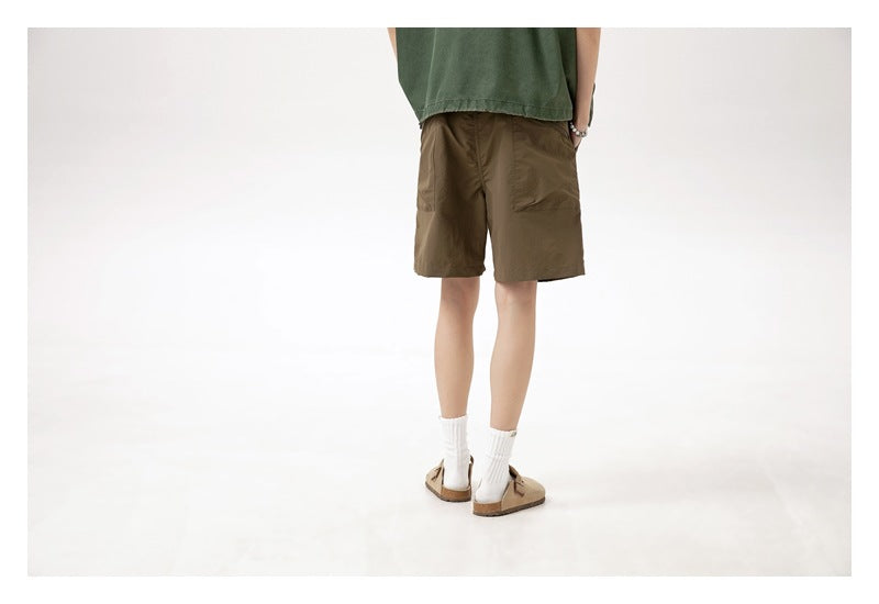 Rear view of a model wearing brown knee-length shorts, a green top, white socks and tan sandals.