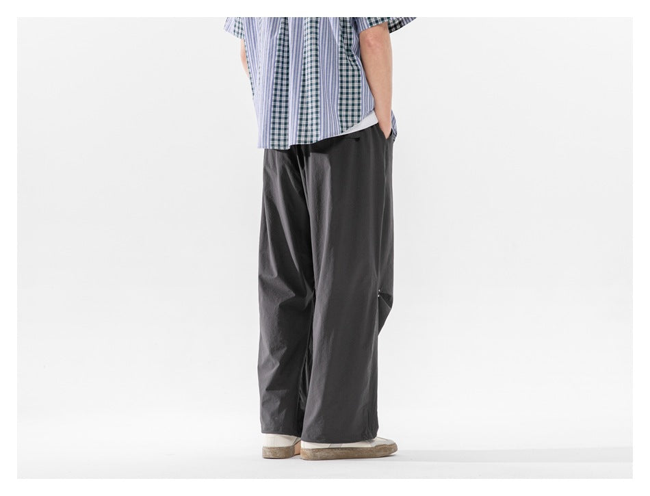 Rear view of a cropped model wearing loose charcoal-gray trousers with a relaxed, straight leg.
