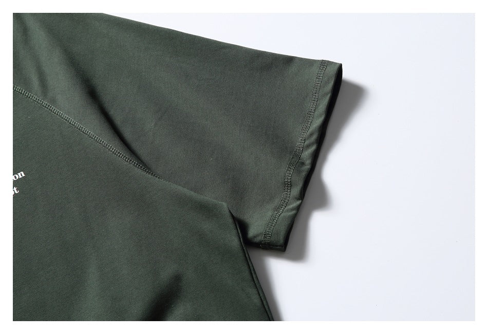 Close-up of the dark green T-shirt's short sleeve and stitched seam on a white background.