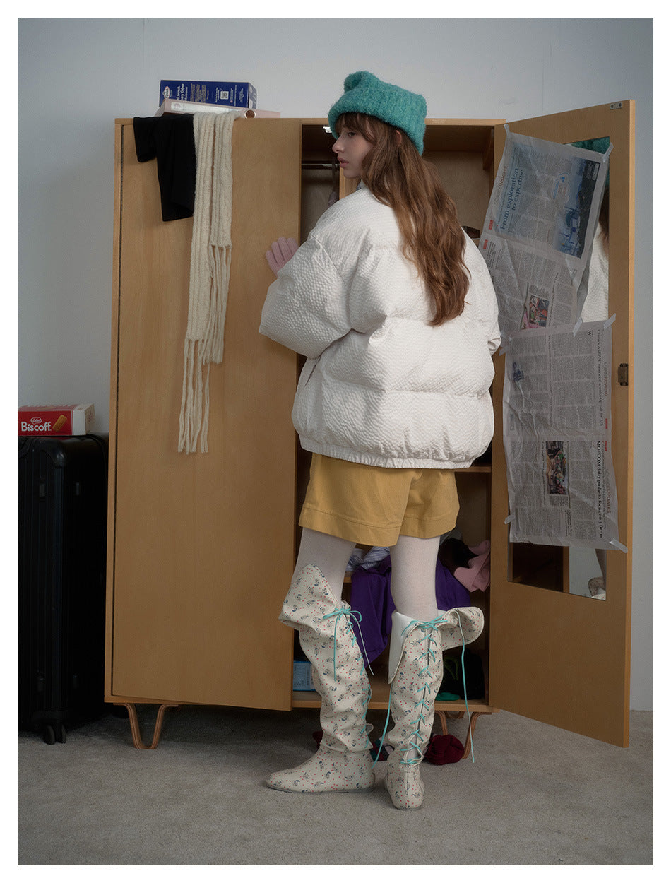 Back view of a model wearing a white quilted jacket, mustard shorts, patterned boots and a teal hat.