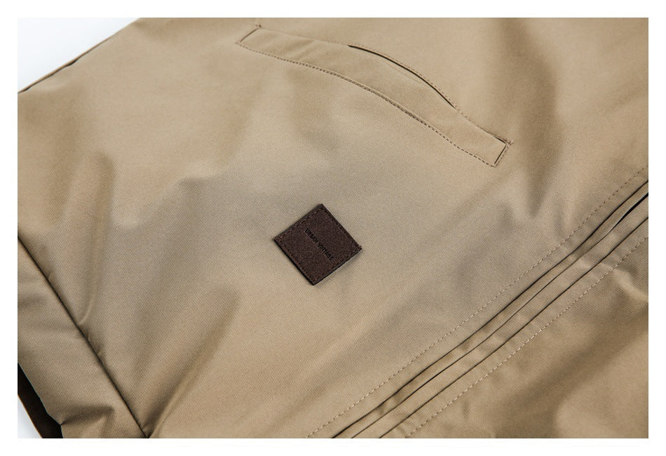 Close-up of a tan garment with a slanted pocket, stitched pleats, and a small dark brown fabric label.