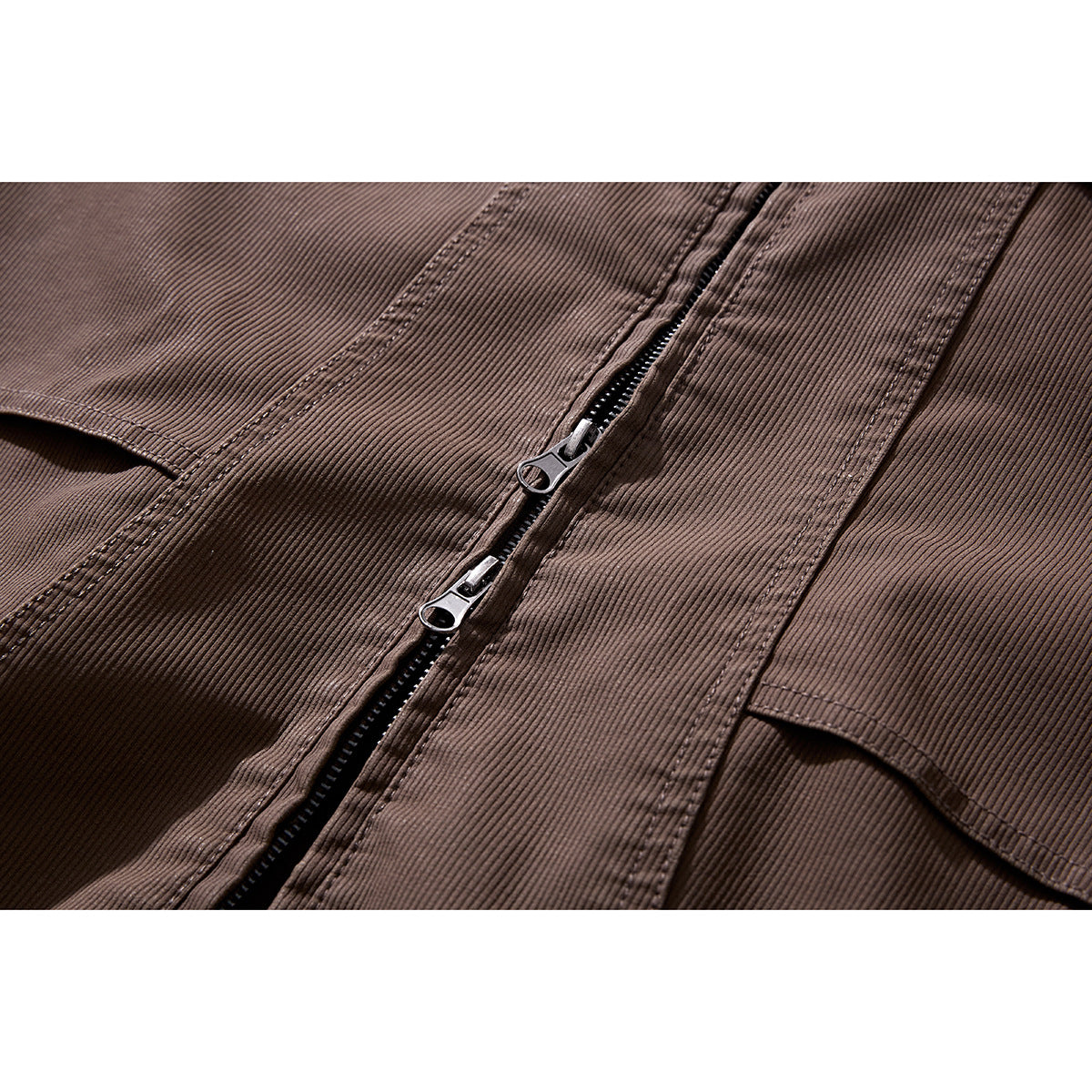 Close-up of a brown jacket's front zipper with two pulls and adjacent stitched pockets.
