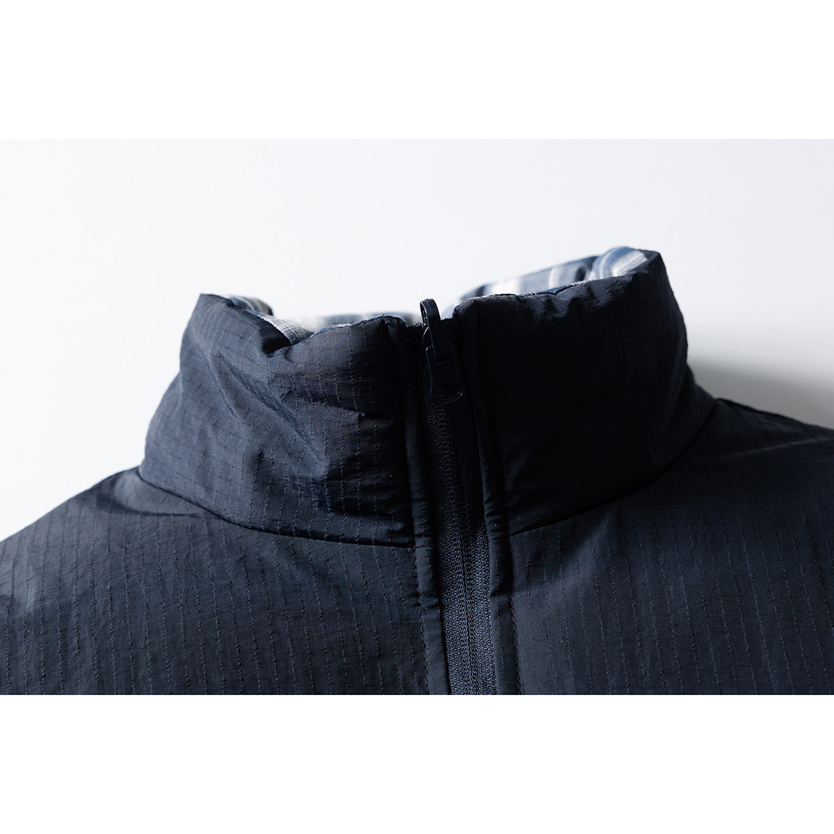 Close-up of a dark jacket’s high collar, central zipper, and subtle stitched texture.