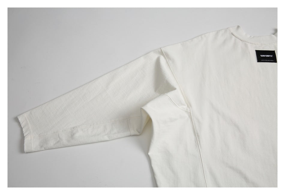 Partial flat lay of an off-white T-shirt showing its long sleeve and black sewn neckline label.