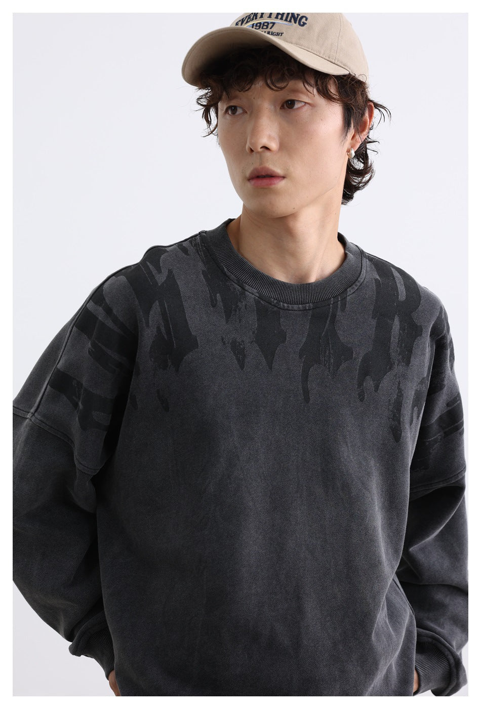 Close view of a model wearing a charcoal sweatshirt with dark graphic detailing across the shoulders and chest.