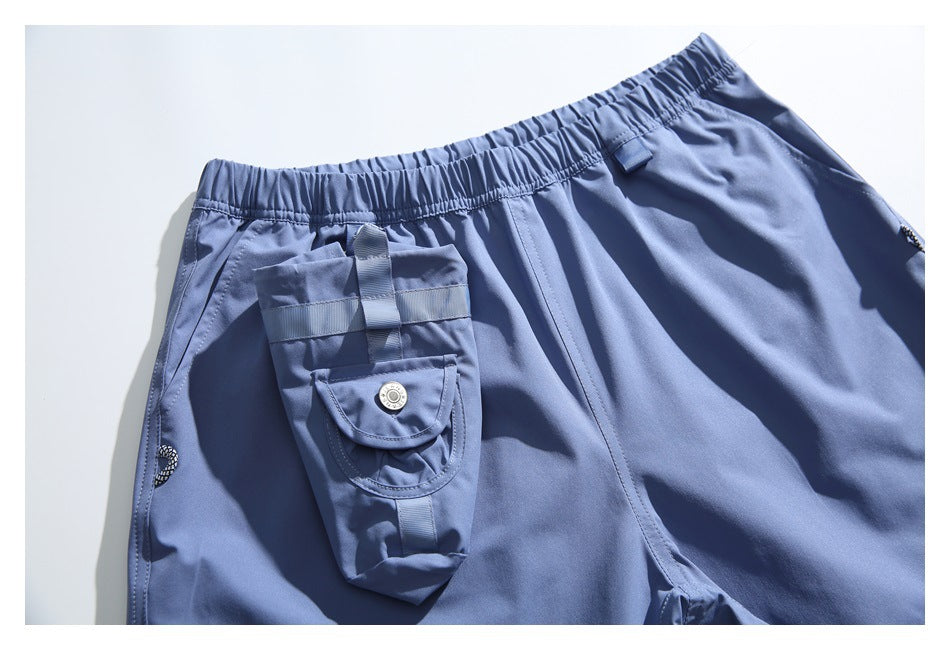 Close view of blue shorts laid flat, showing an elastic waist and a large strapped cargo pocket with a snap flap.