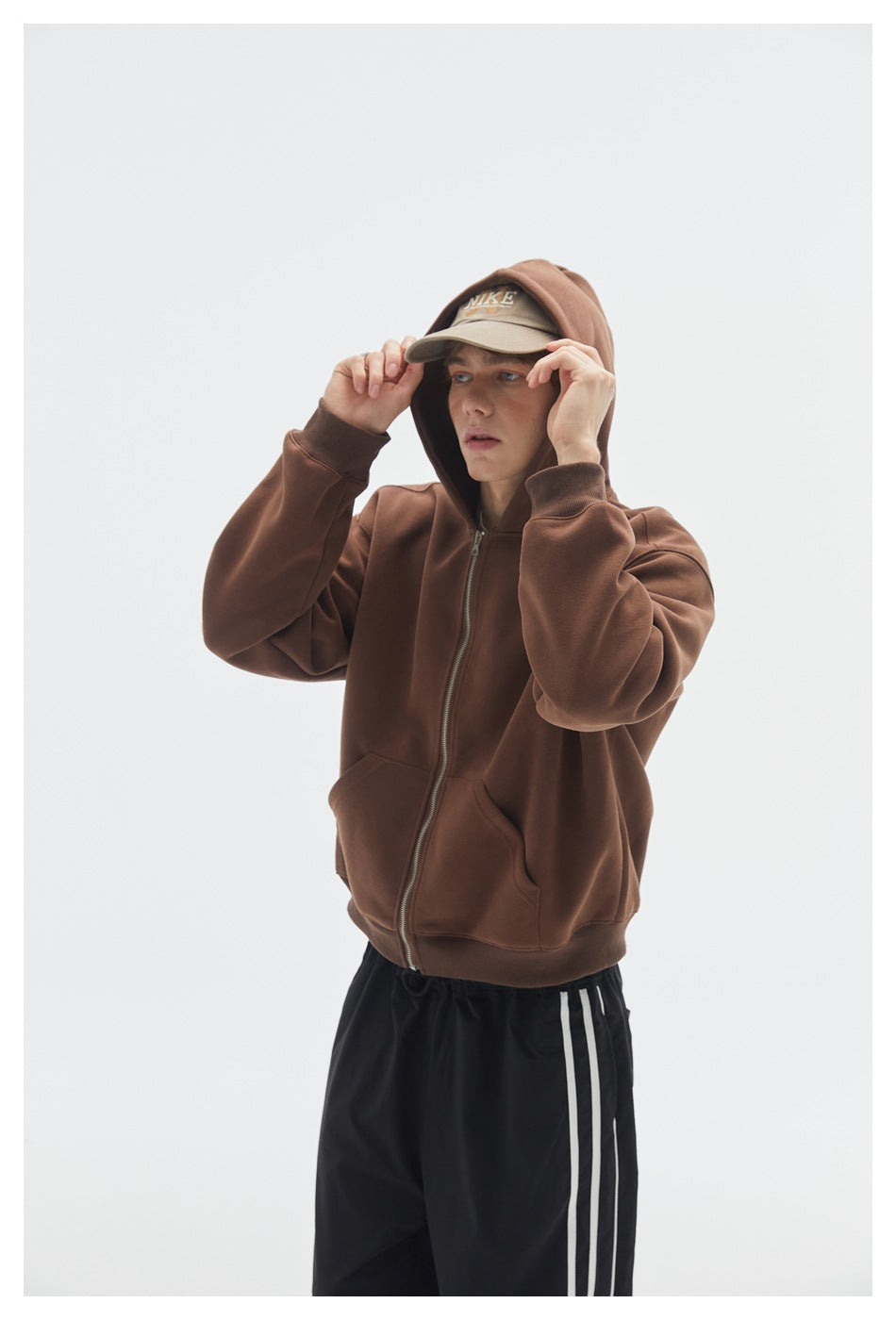 Close view of a model wearing a brown zip-up hoodie with a hood and front pockets.