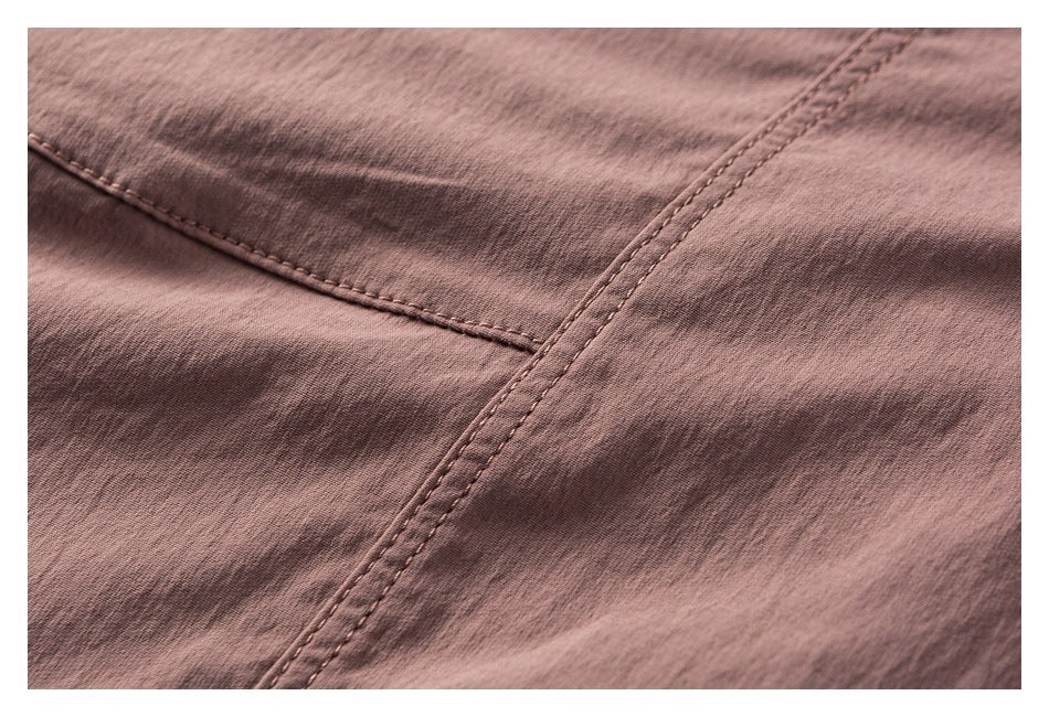 Close-up of dusty mauve jacket fabric and intersecting double-stitched seams.