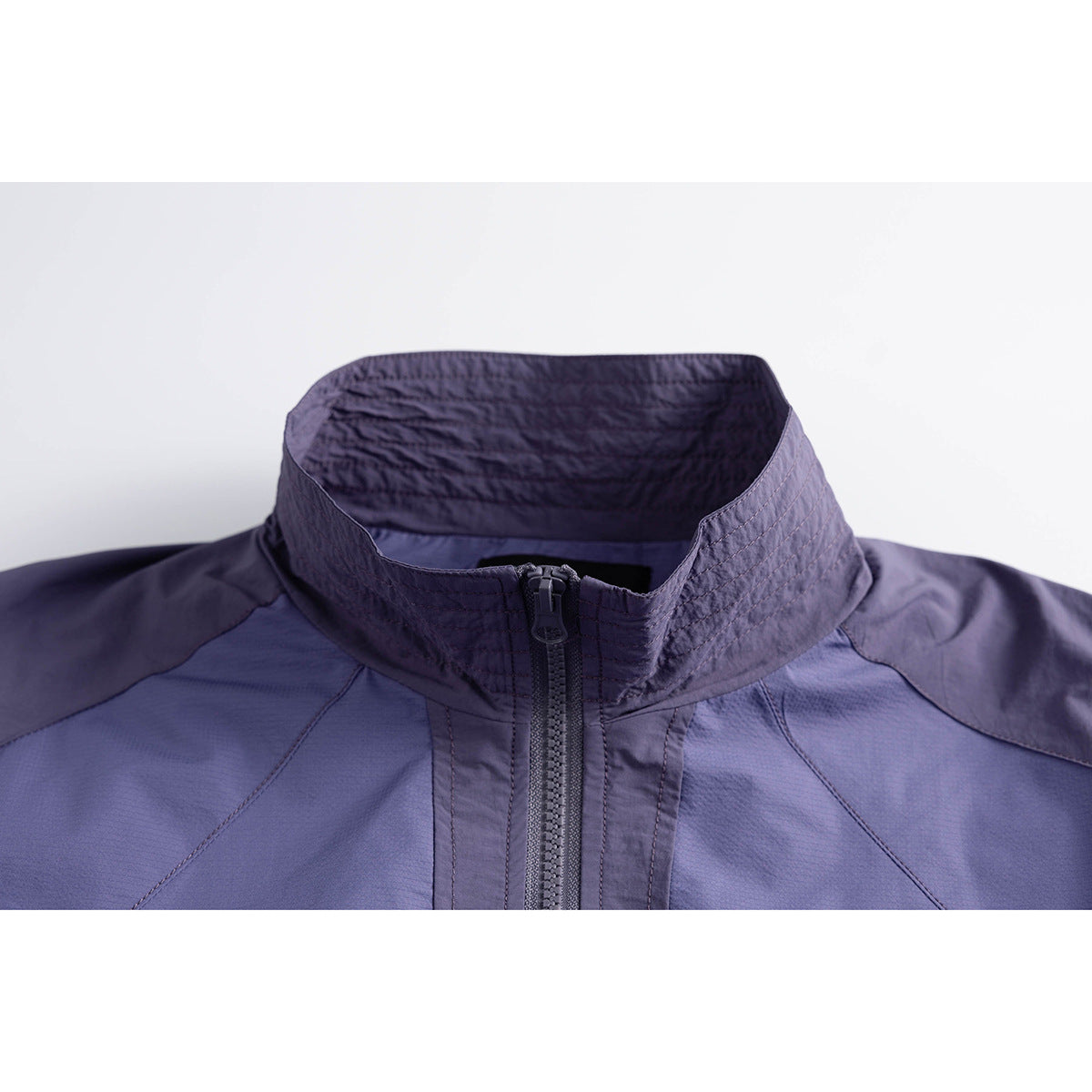 Close-up of a blue-violet jacket collar, dark contrast panels, stitching, and front zipper.