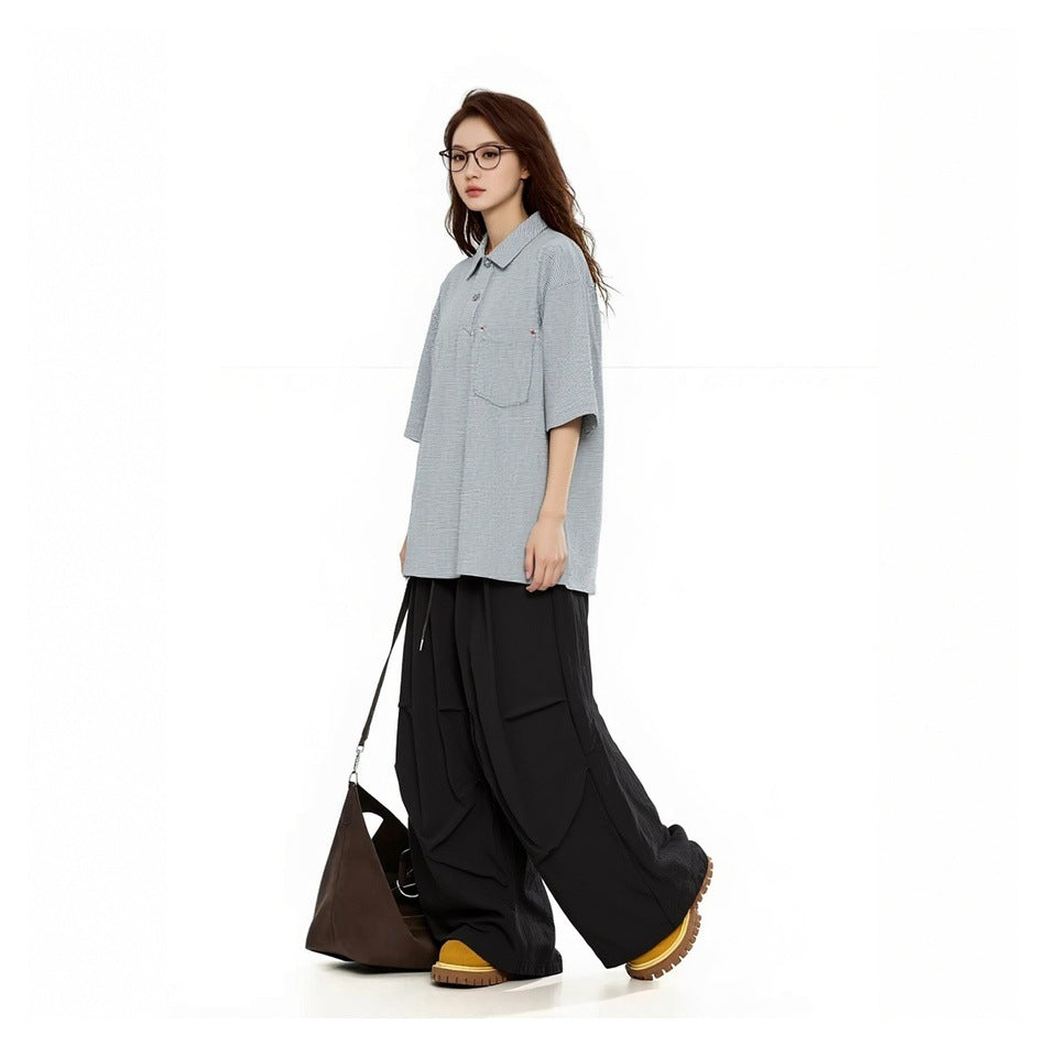 Model wearing gray-white striped polo shirt with black wide-leg pants and a brown shoulder bag