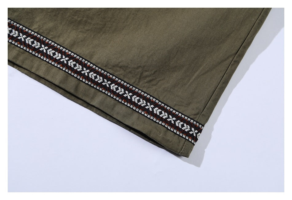 Close-up of the olive shirt hem with a black, white, and rust geometric trim band.