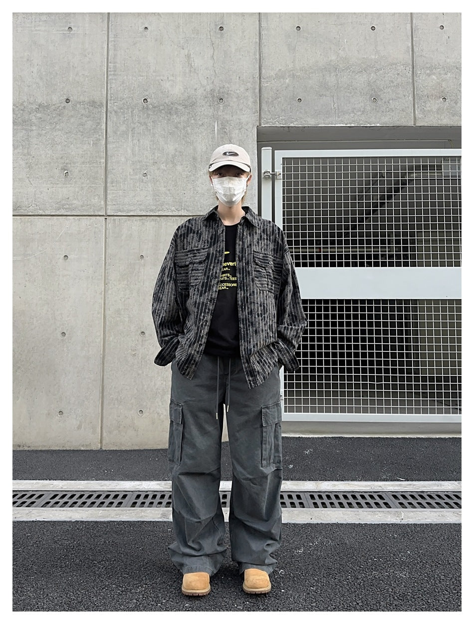 Full-length model wearing loose charcoal cargo pants with thigh pockets and a dark striped button-up shirt.