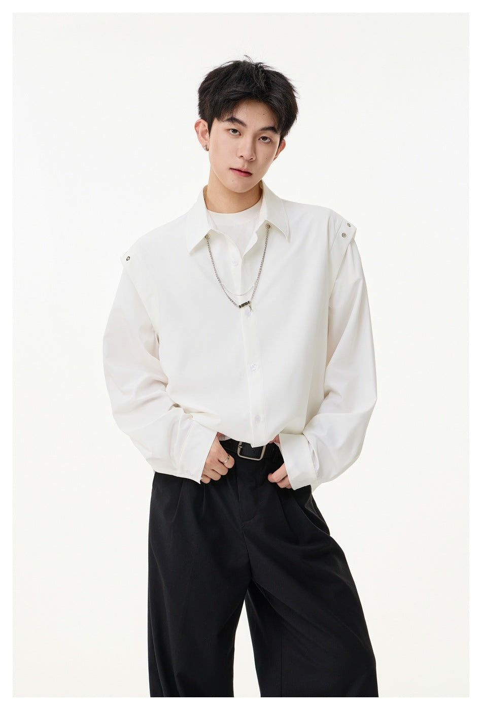 Model wearing a white oversized button-up shirt with shoulder snaps and a silver chain, paired with black trousers.