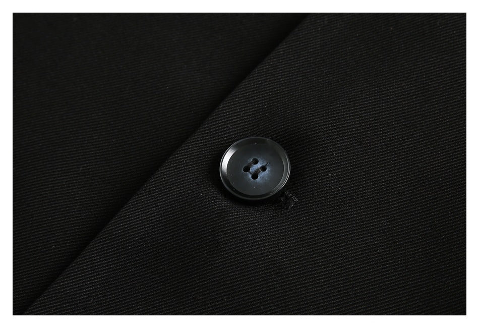 Close-up of a black four-hole button on black garment fabric.