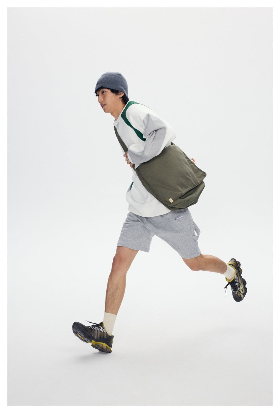 Model running in light gray shorts with a side utility loop, carrying an olive bag.