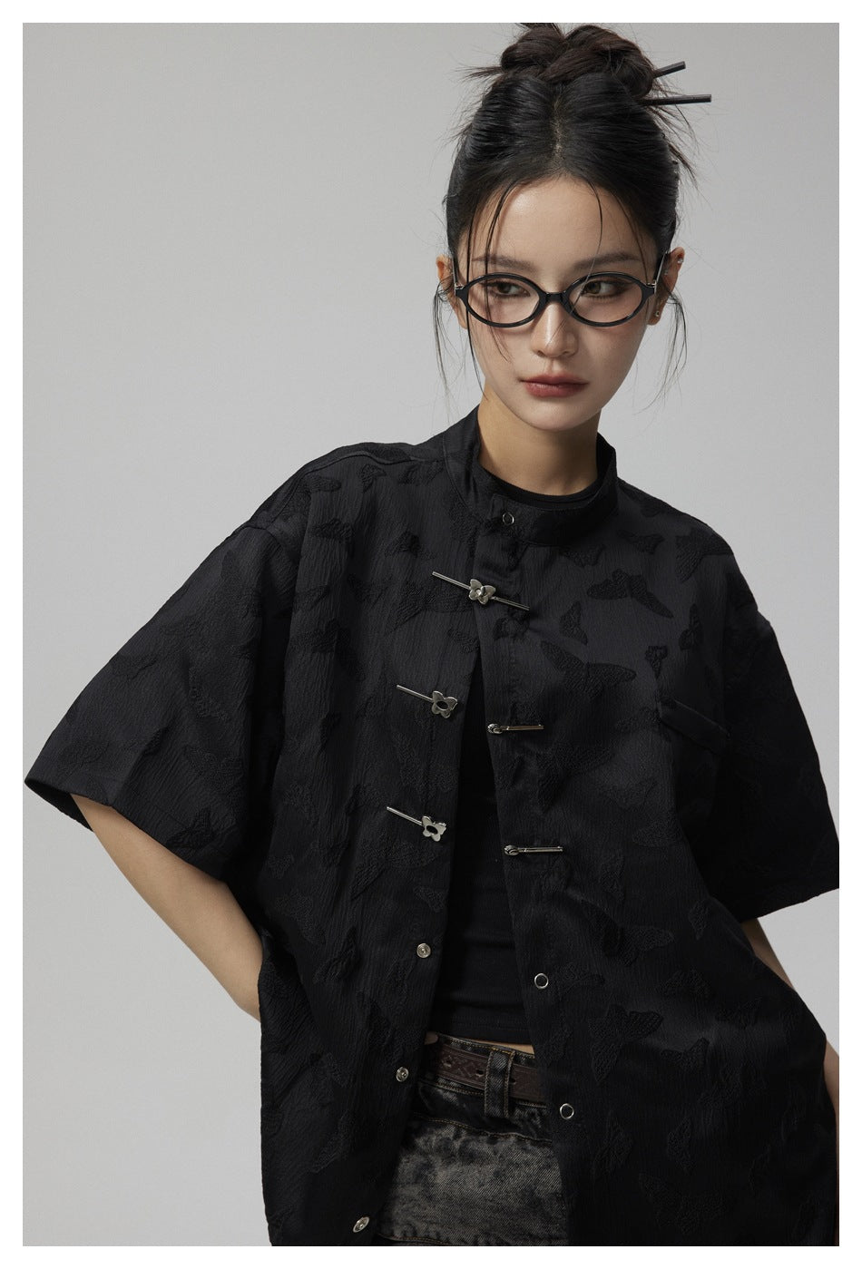 Close view of a model wearing a black butterfly-pattern shirt with a stand collar and silver bar closures.