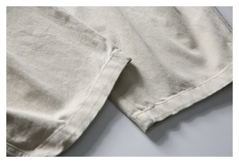 Close-up of the stitched hem and folded edge of light beige trouser legs.