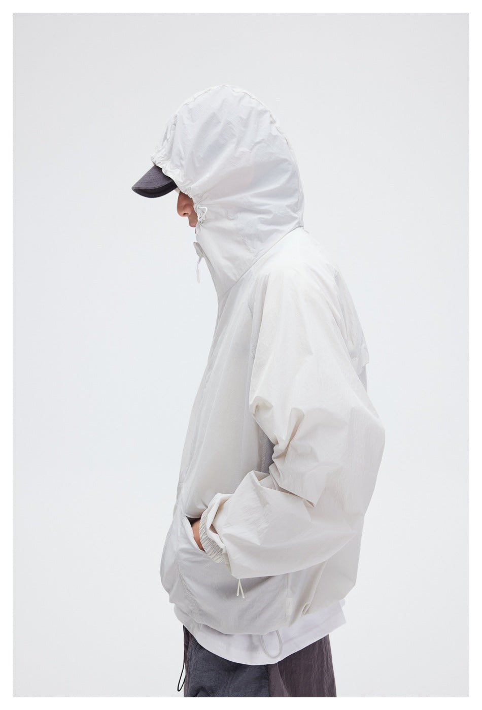 Side view of a model wearing the white jacket with its hood raised and drawcords visible.