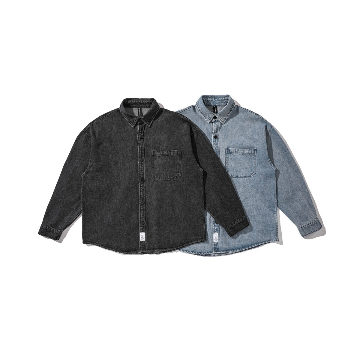 Two long-sleeve denim shirts shown from the front, charcoal black in front and light blue behind, each with a chest pocket.