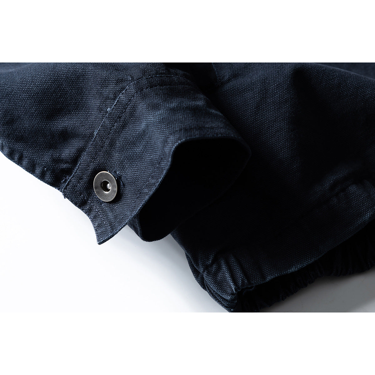 Close-up of a dark navy jacket sleeve cuff with a metal snap and gathered hem visible.