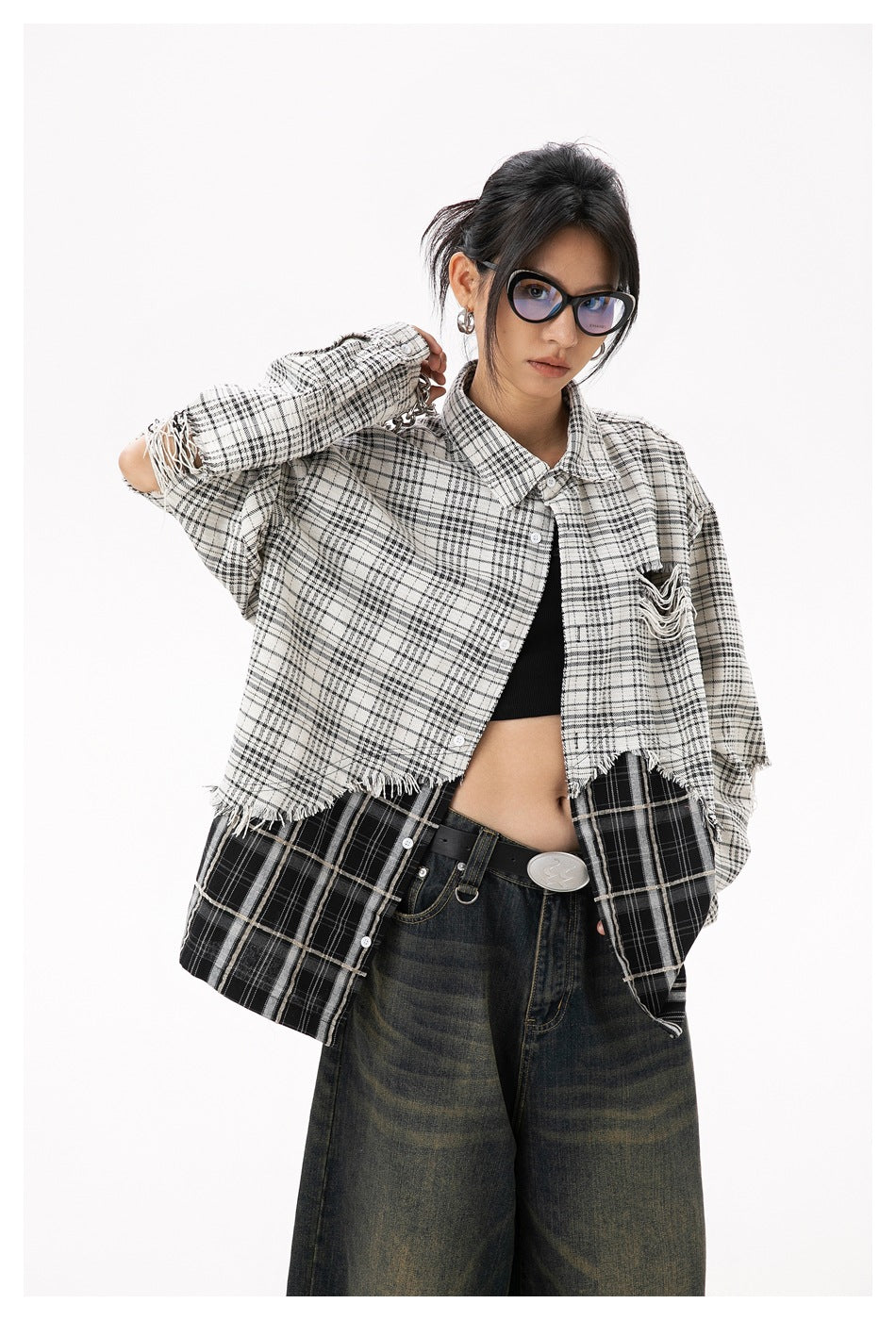 Model wearing an oversized black-and-white plaid shirt with frayed panels over a black top and dark jeans.