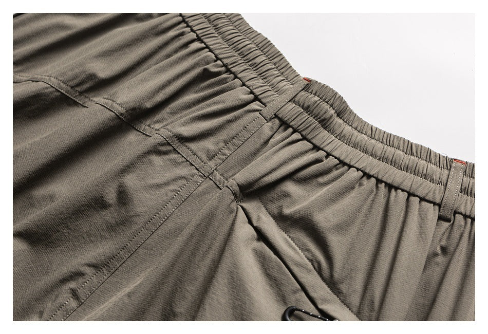 Close-up of taupe trousers showing the gathered waistband, belt loops, and rear seam details.