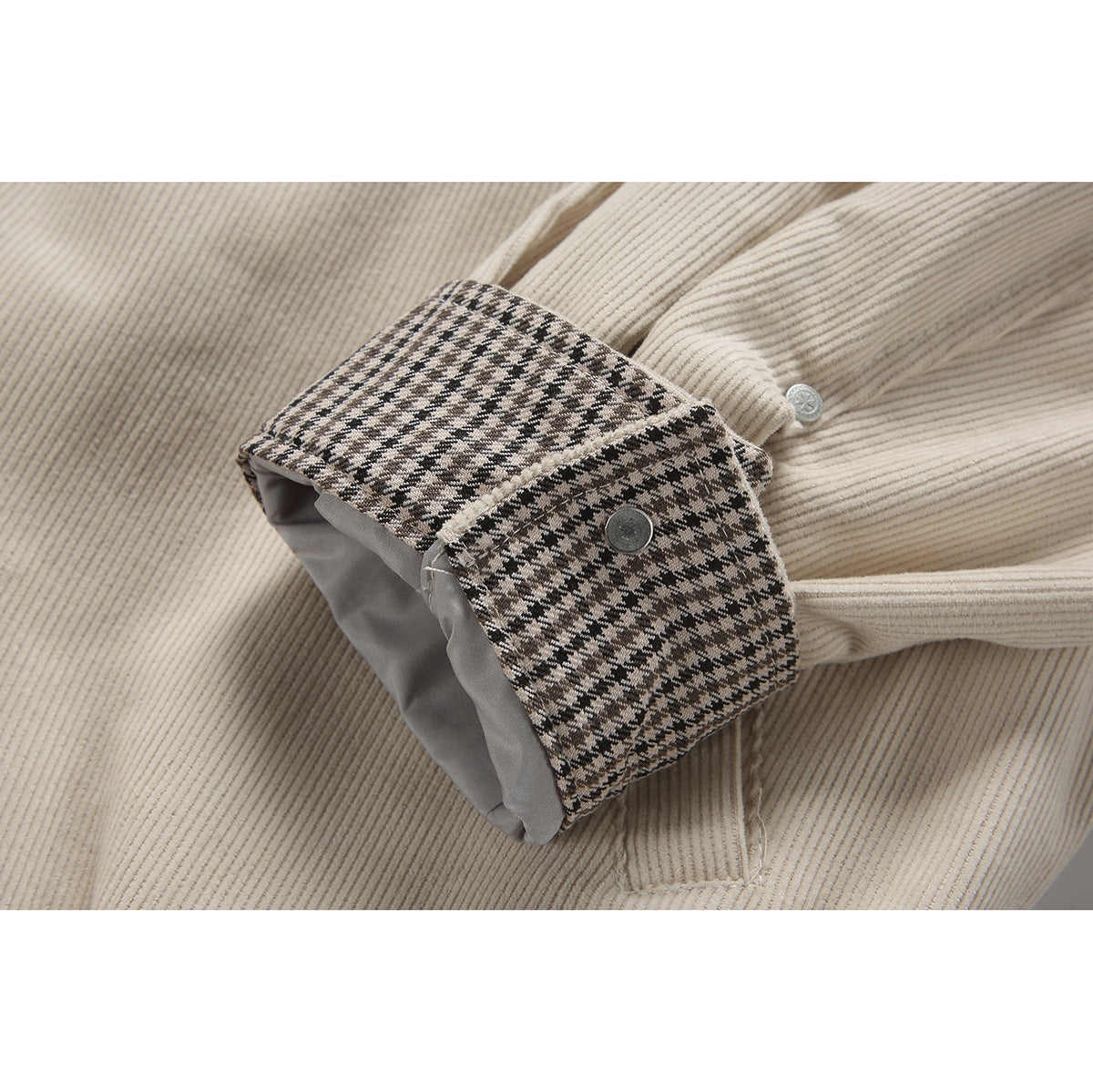 Close-up of a beige jacket cuff with a black-and-beige checked lining and snap button.