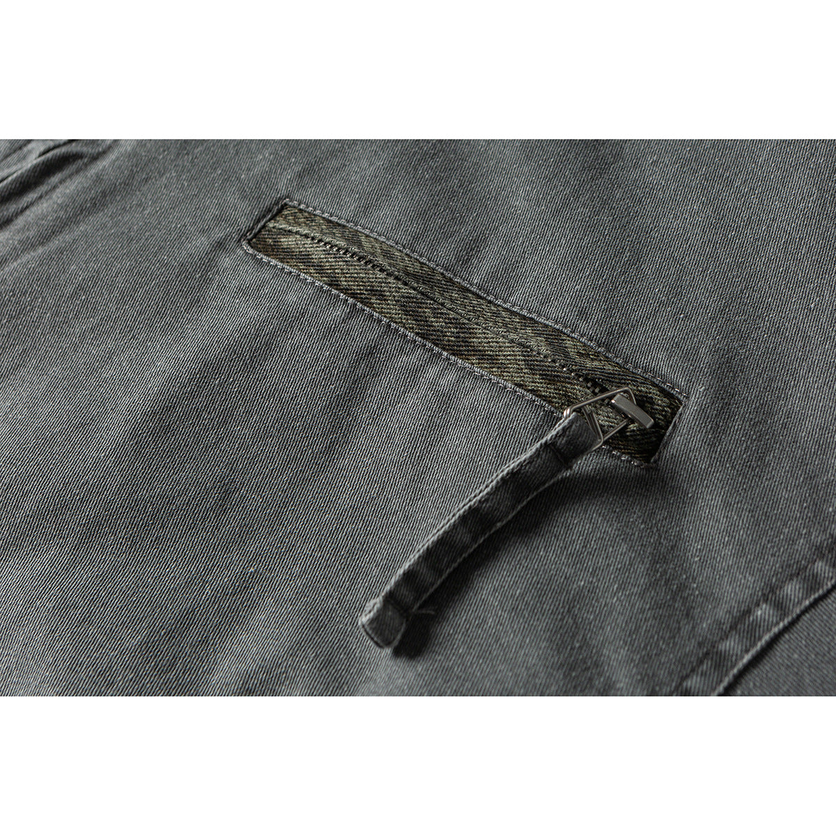 Close-up of a narrow olive-patterned welt pocket and hanging fabric tab on a gray jacket.