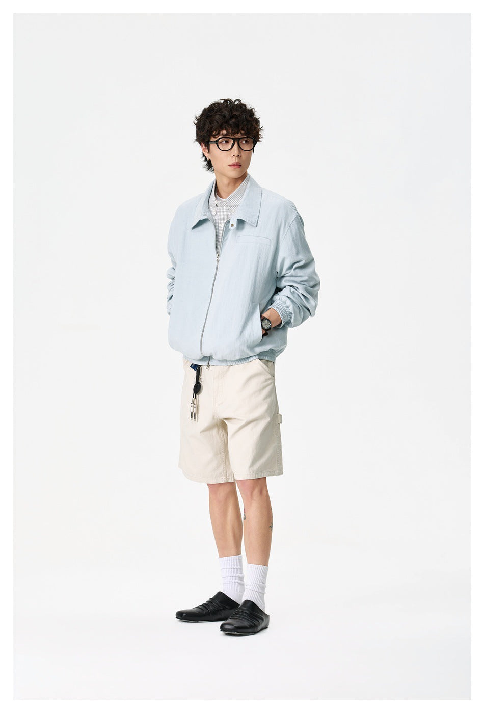 Full-length model wearing a pale blue collared jacket with cream shorts against a plain white background.
