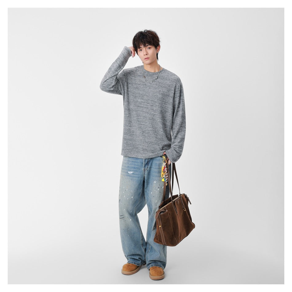 Full-length model wearing a marled gray crew-neck sweater and loose light-wash jeans, carrying a brown bag.