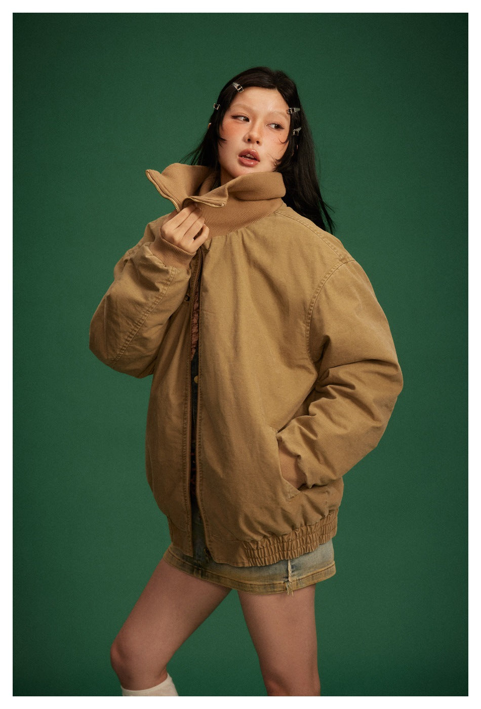 Model wears a camel-brown oversized jacket zipped partway, with its tall ribbed collar turned up.